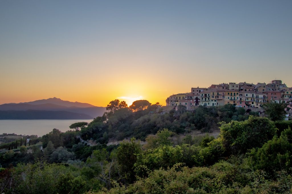 Sonnenuntergang über einem Hügel mit Häusern und Blick auf das Meer.