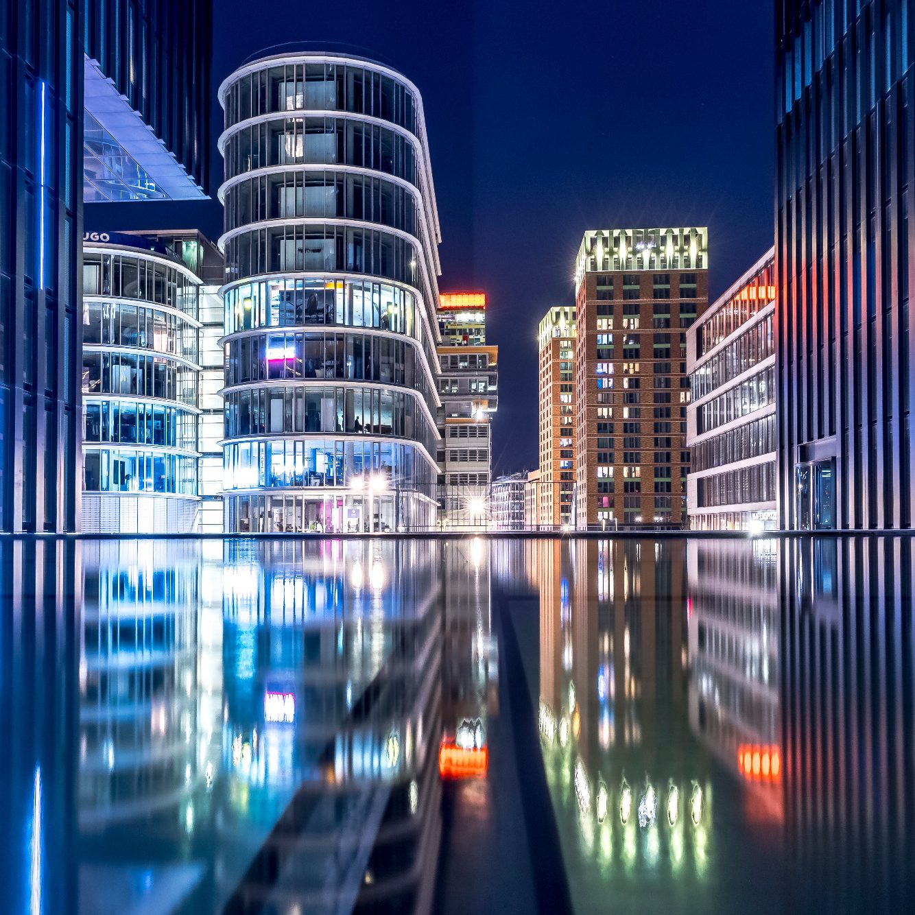 City view at night with modern buildings and reflective surfaces.