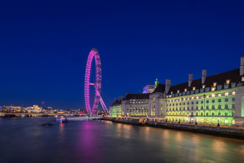 Das London Eye leuchtet pink, daneben die beleuchtete Uferpromenade.