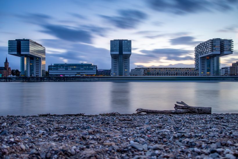 Modern buildings on the water at dawn, standing behind a gravel bay.