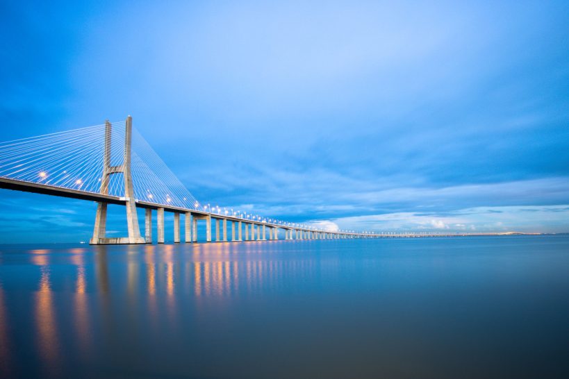 Modern suspension bridge at sunset with reflective water.