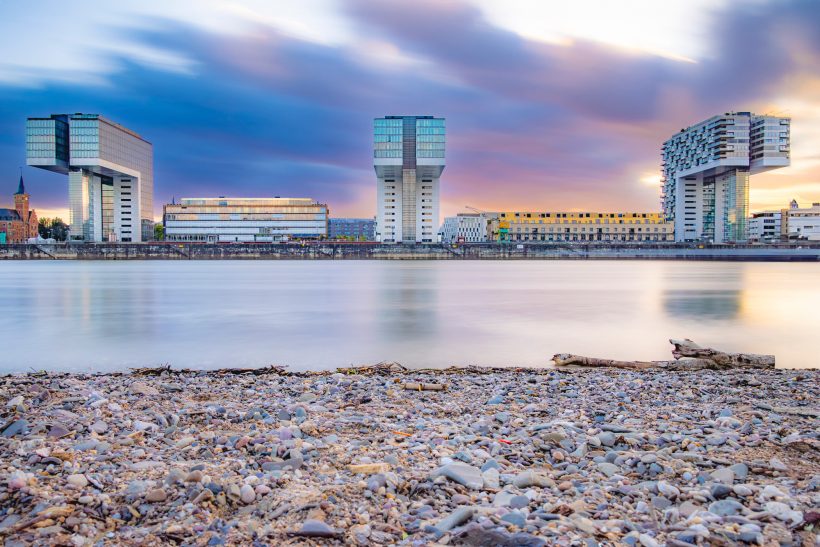 Modern buildings by the water with lively clouds and soft evening light.