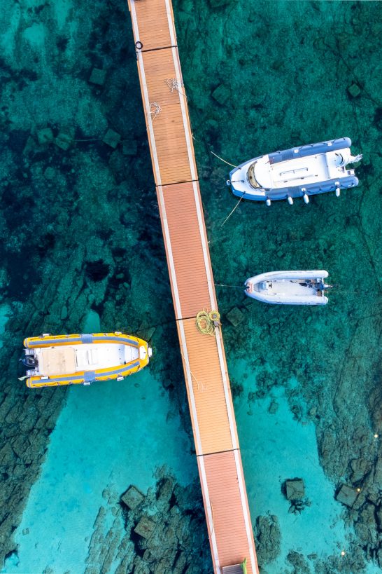 Wooden bridge over clear water with several boats in the harbour area.