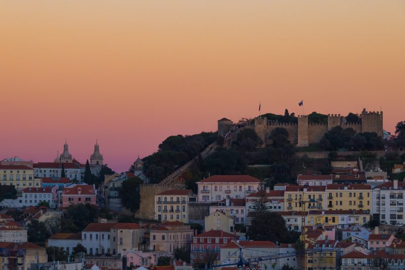 Blick auf die Stadt mit Sonnenuntergang und einer Burg auf einem Hügel.