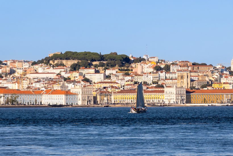 Segelboot auf dem Wasser mit Blick auf die Stadt und Hügel im Hintergrund.