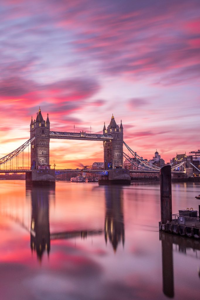 Tower Bridge at sunrise with colorful clouds and reflective water.