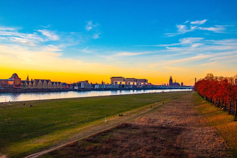 Sunset over a river, with buildings and colorful trees on the shore.