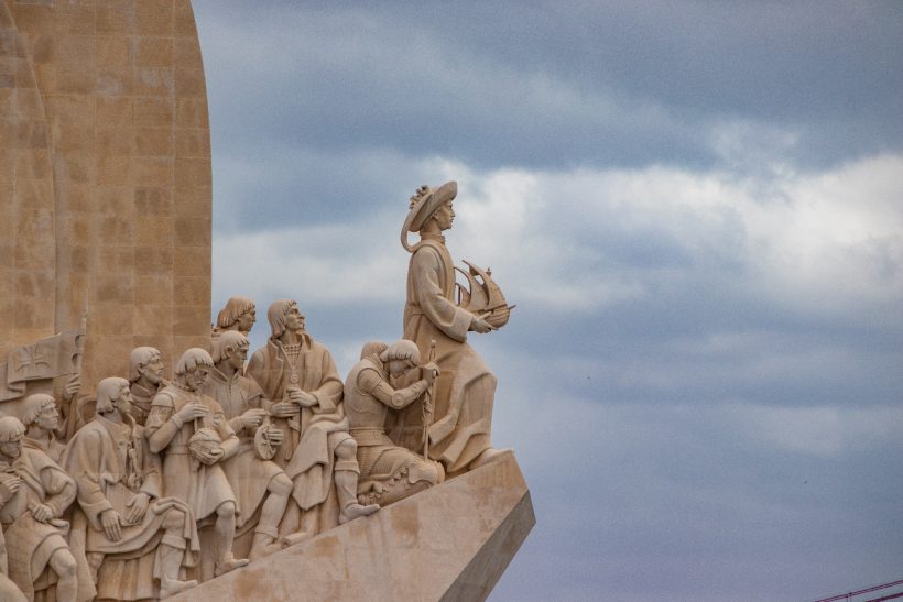 Sculpture of a figure holding a ship surrounded by other stylized figures.