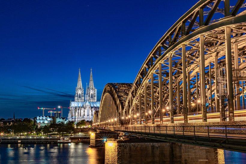 Cologne Cathedral in the background, illuminated Hohenzollern Bridge at night.