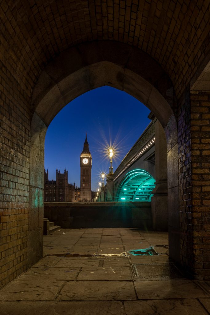 View through an arc over the Thames at night with Big Ben in the background.