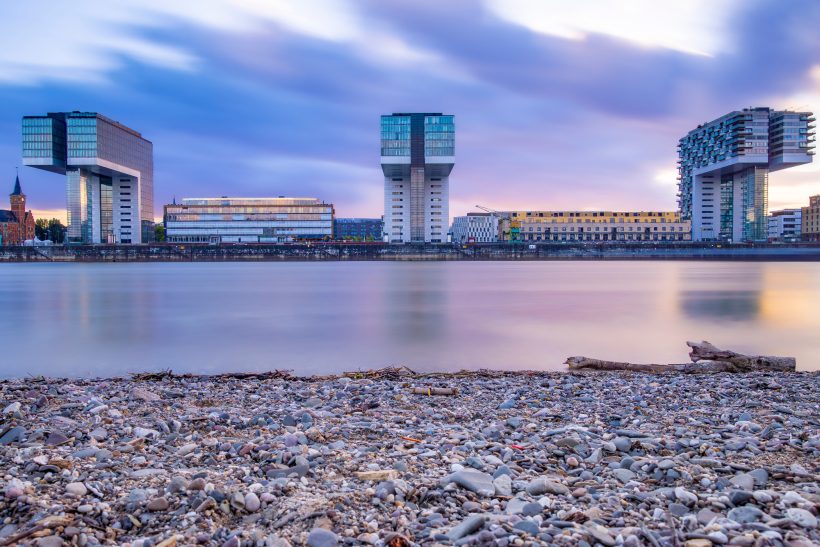 Drei moderne Gebäude am Ufer eines ruhigen Gewässers bei Sonnenuntergang.