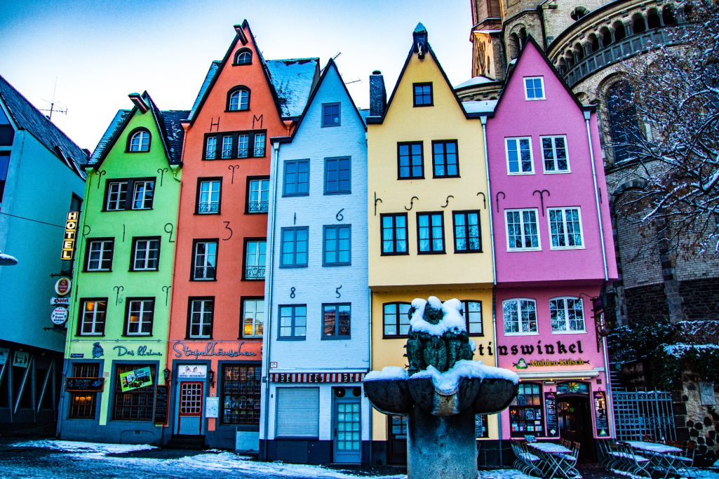 Colorful, historic building in a town with a fountain in the foreground.