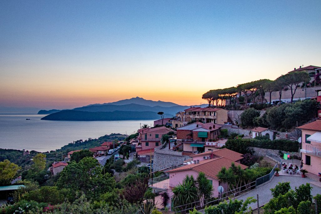 Sunset over a coastal town with mountains in the background.