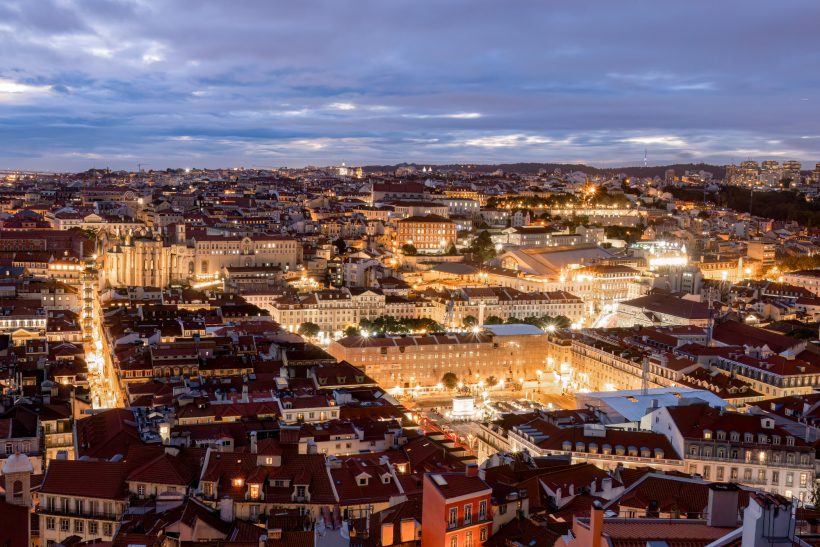 Panoramic views of Lisbon at night with illuminated squares and roofs.